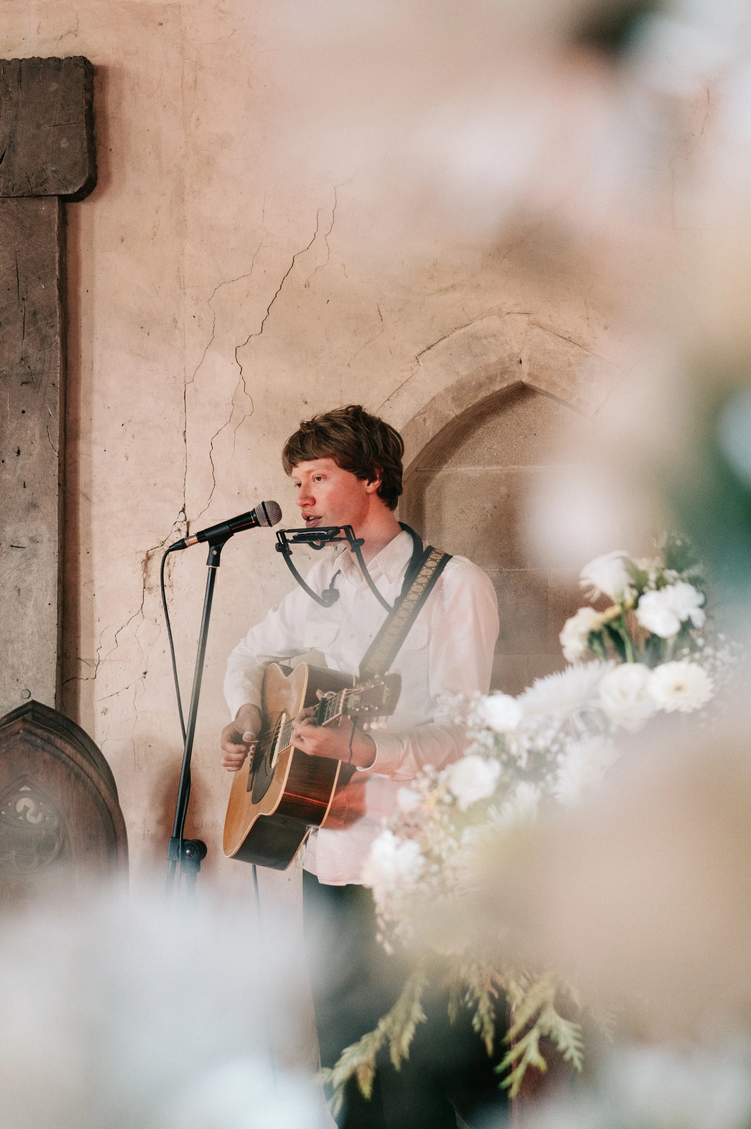 A singer with an acoustic guitar performs during the ceremony, framed by white flowers