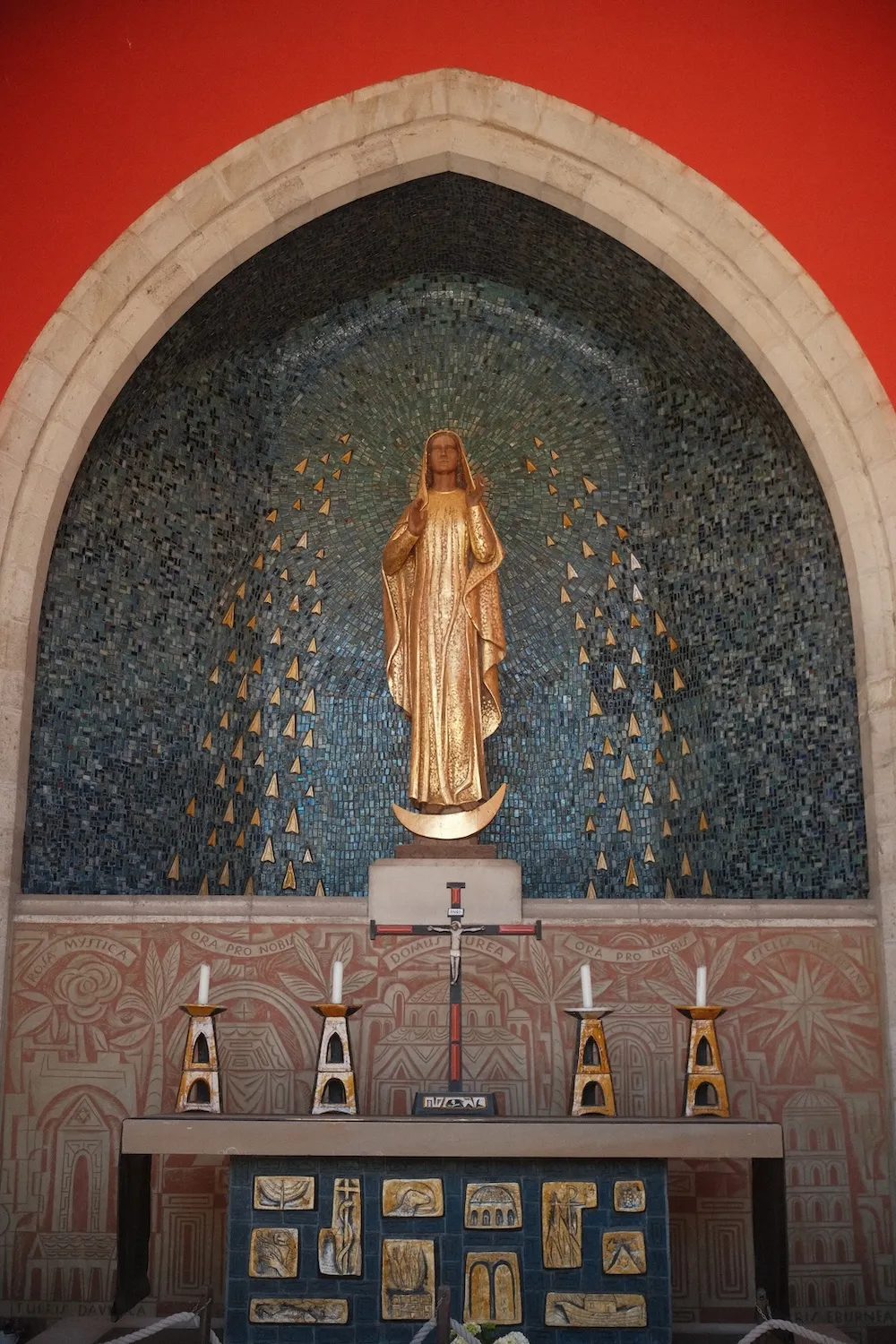 A gilded statue of Our Lady standing on a crescent moon, in a blue mosaic niche above a chapel altar at The Friars