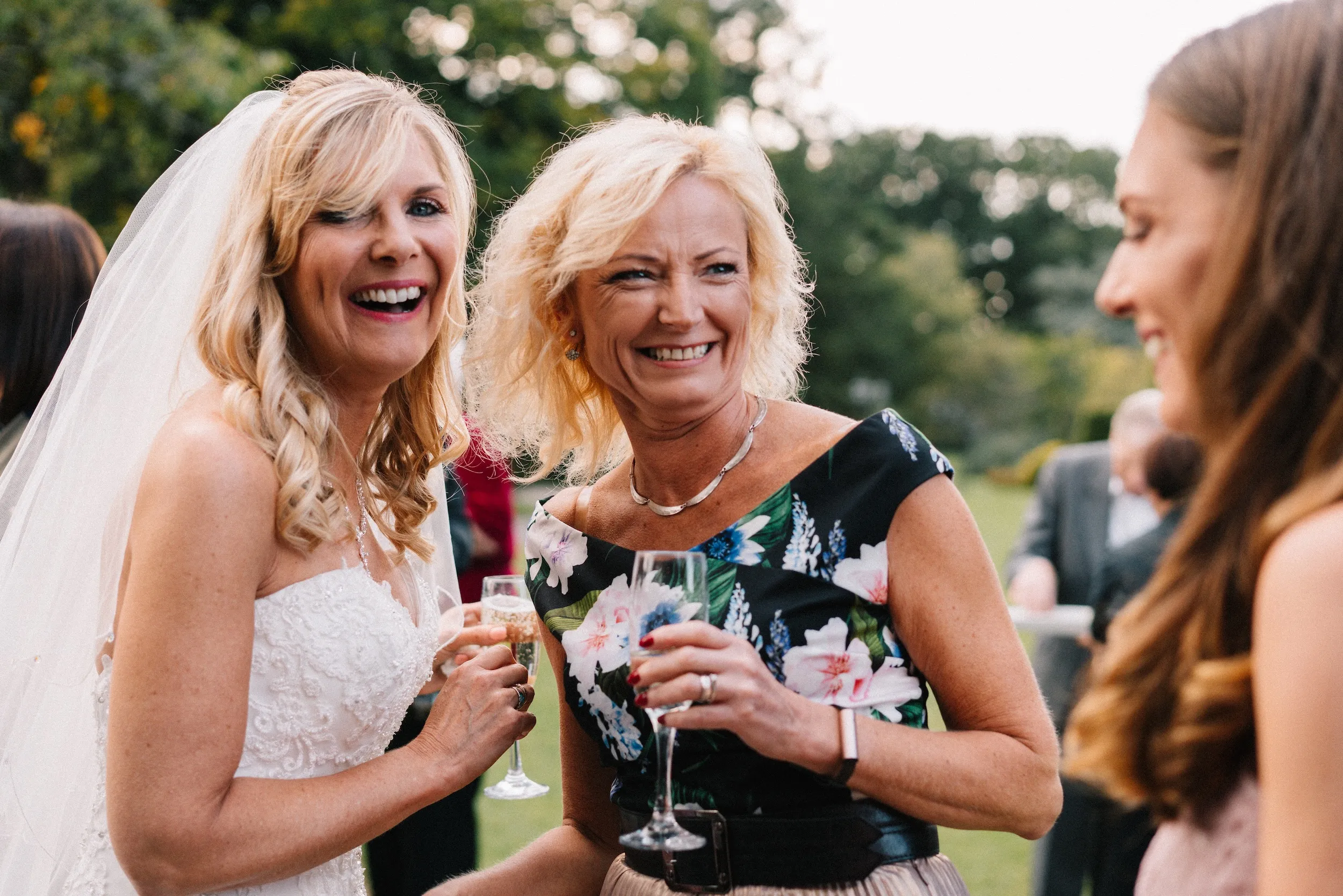 Fiona and a friend laugh with glasses in hand on the lawn