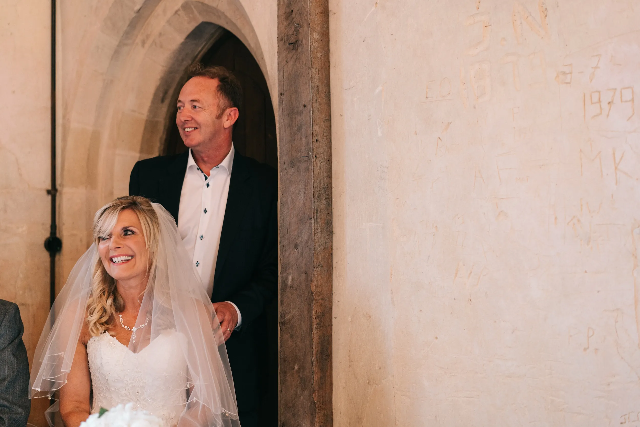 Fiona and Mark smile from a medieval doorway with old graffiti carved into the wall