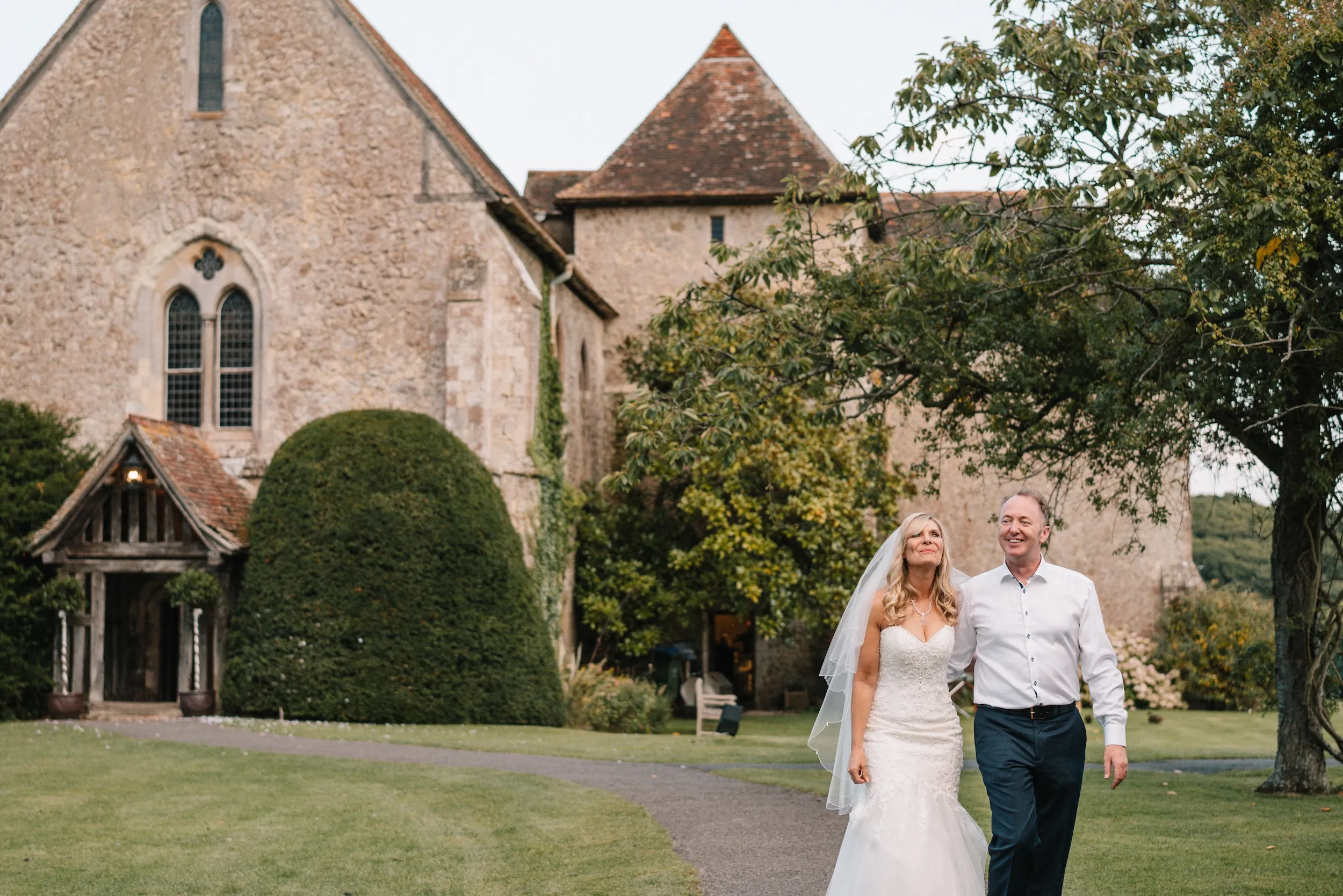 Mark and Fiona walk across the lawn at Bilsington Priory with the priory and church behind them