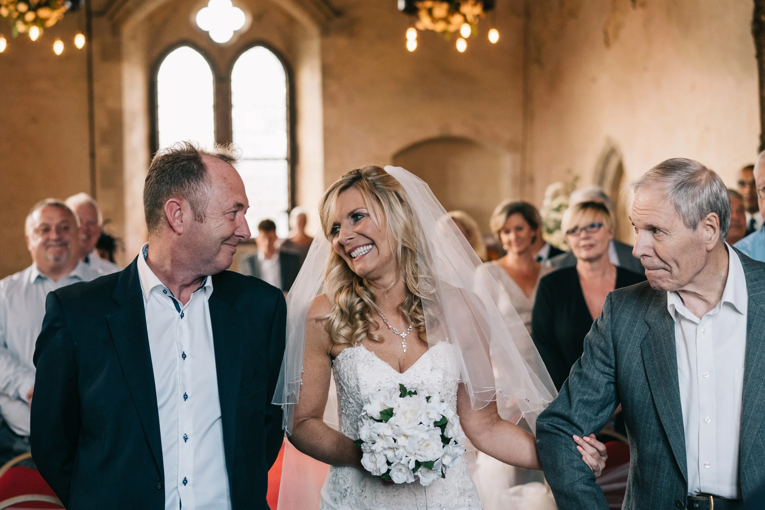 Fiona smiles as she is walked down the aisle of the Great Hall at Bilsington Priory