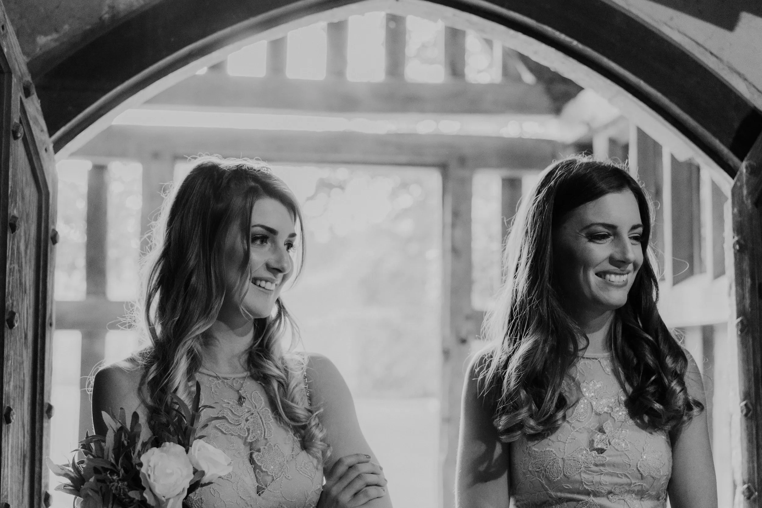 Black and white photograph of two bridesmaids smiling in an arched timber doorway