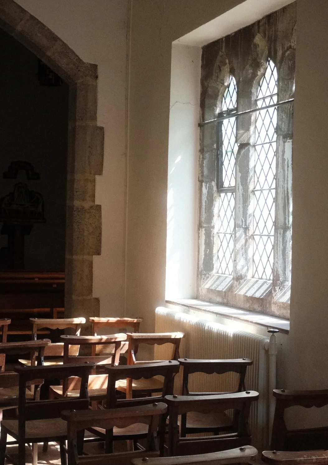 A Catholic chapel at Aylesford Priory, Kent: daylight through a leaded window falls across rows of wooden chairs