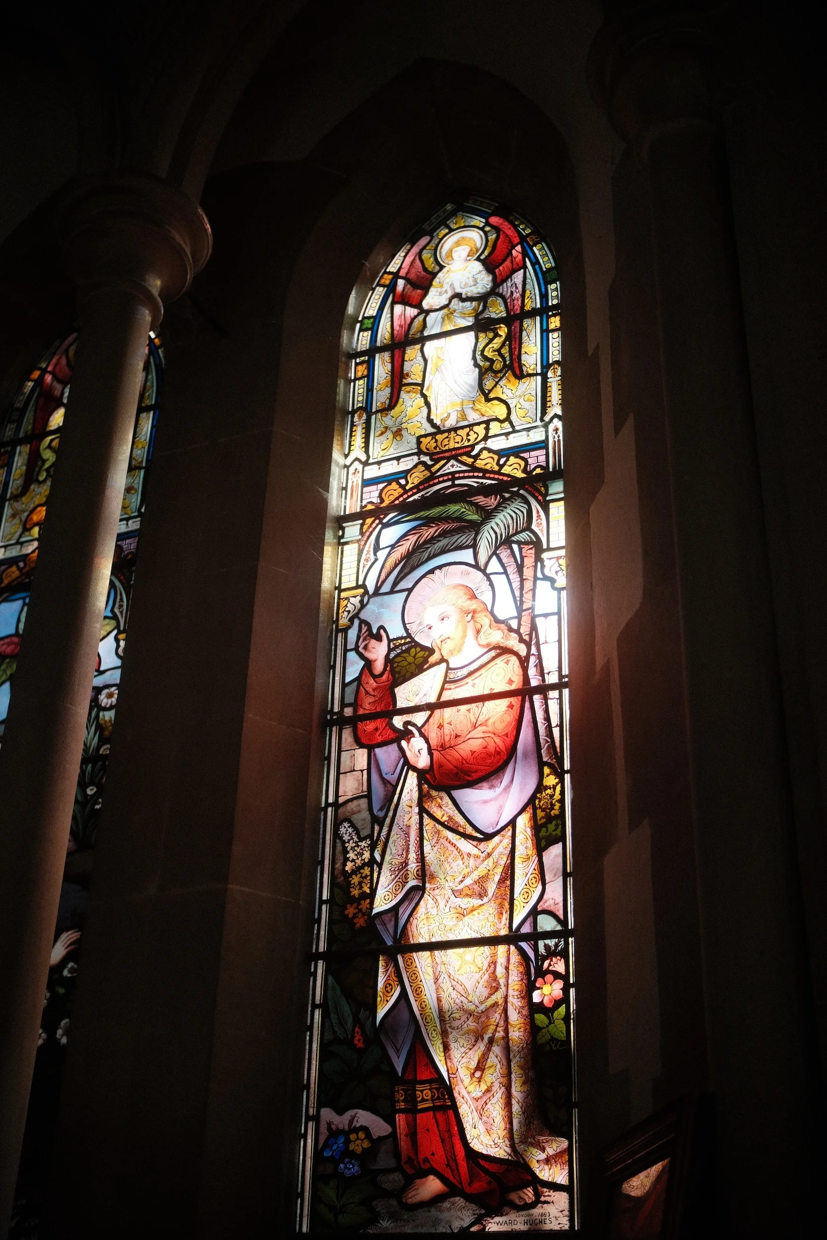 A stained glass window of a saint glowing in a dark church