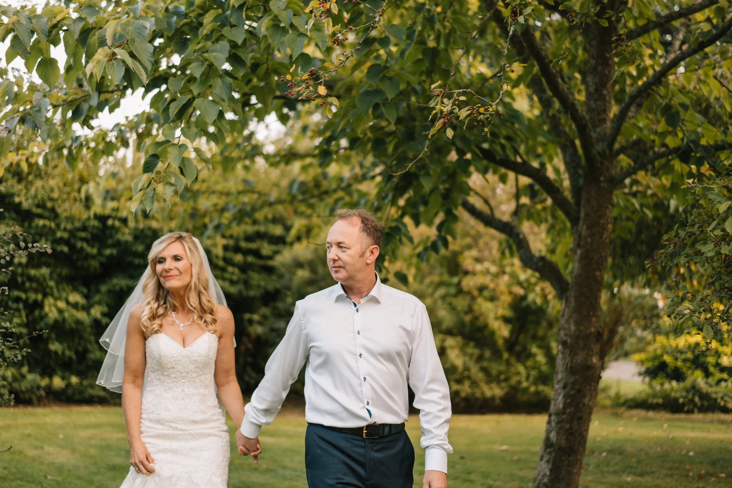 Mark and Fiona walk hand in hand under the trees