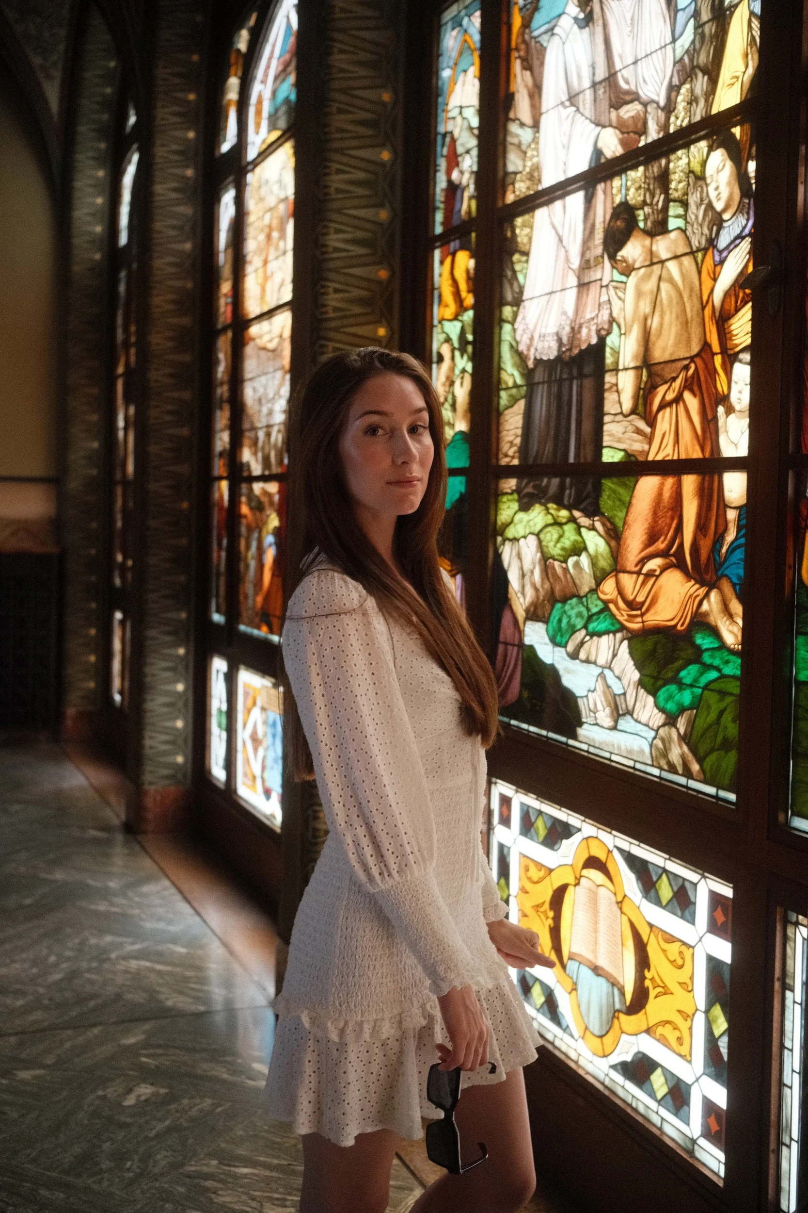 A woman stands beside a tall stained glass window