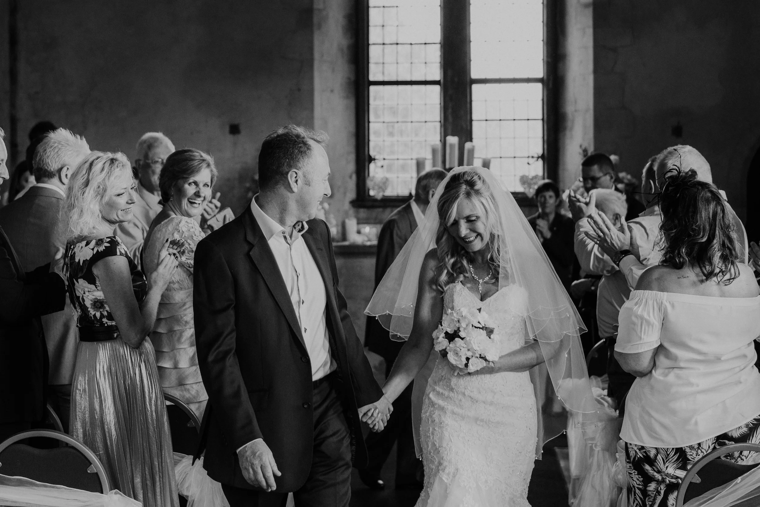 Black and white photograph of Mark and Fiona walking hand in hand through their cheering guests