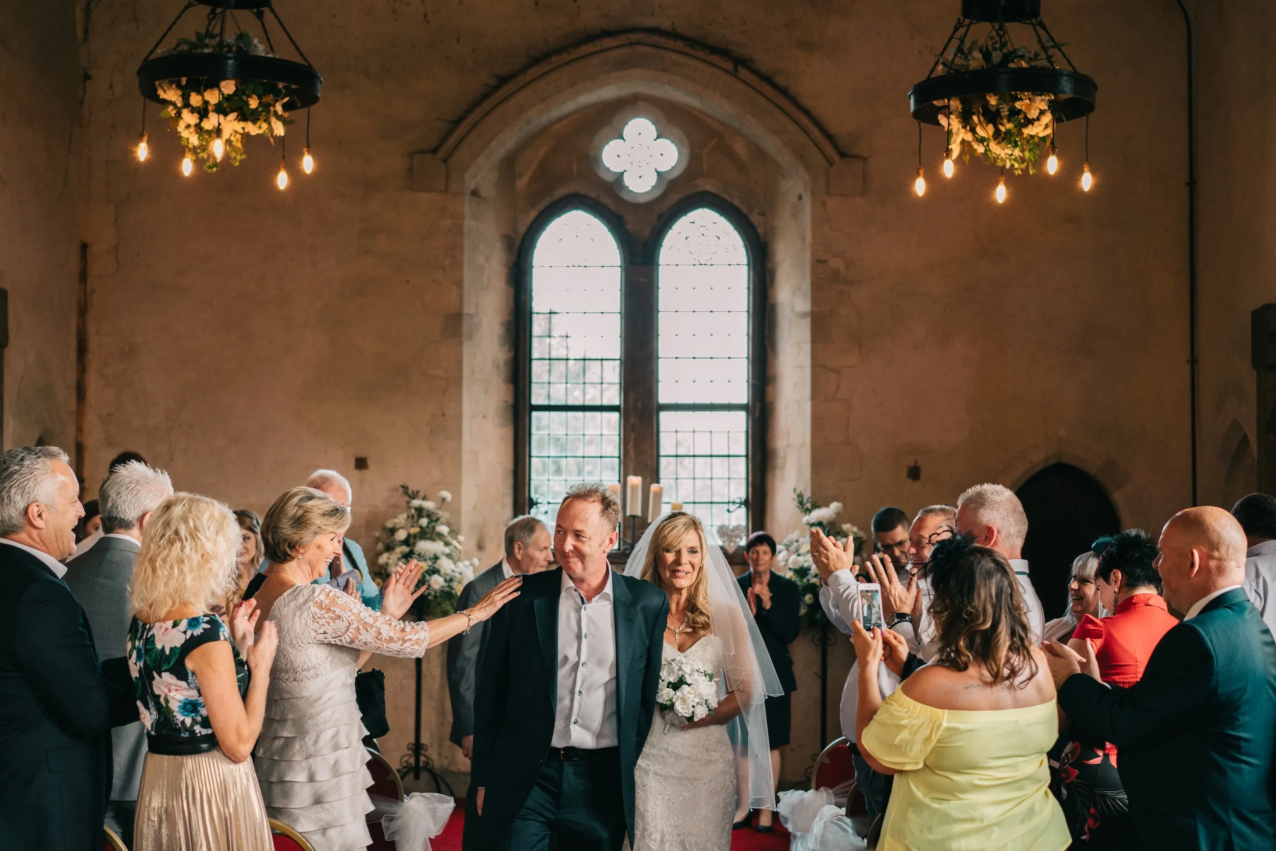 Guests cheer as Mark and Fiona walk back down the aisle under the chandeliers