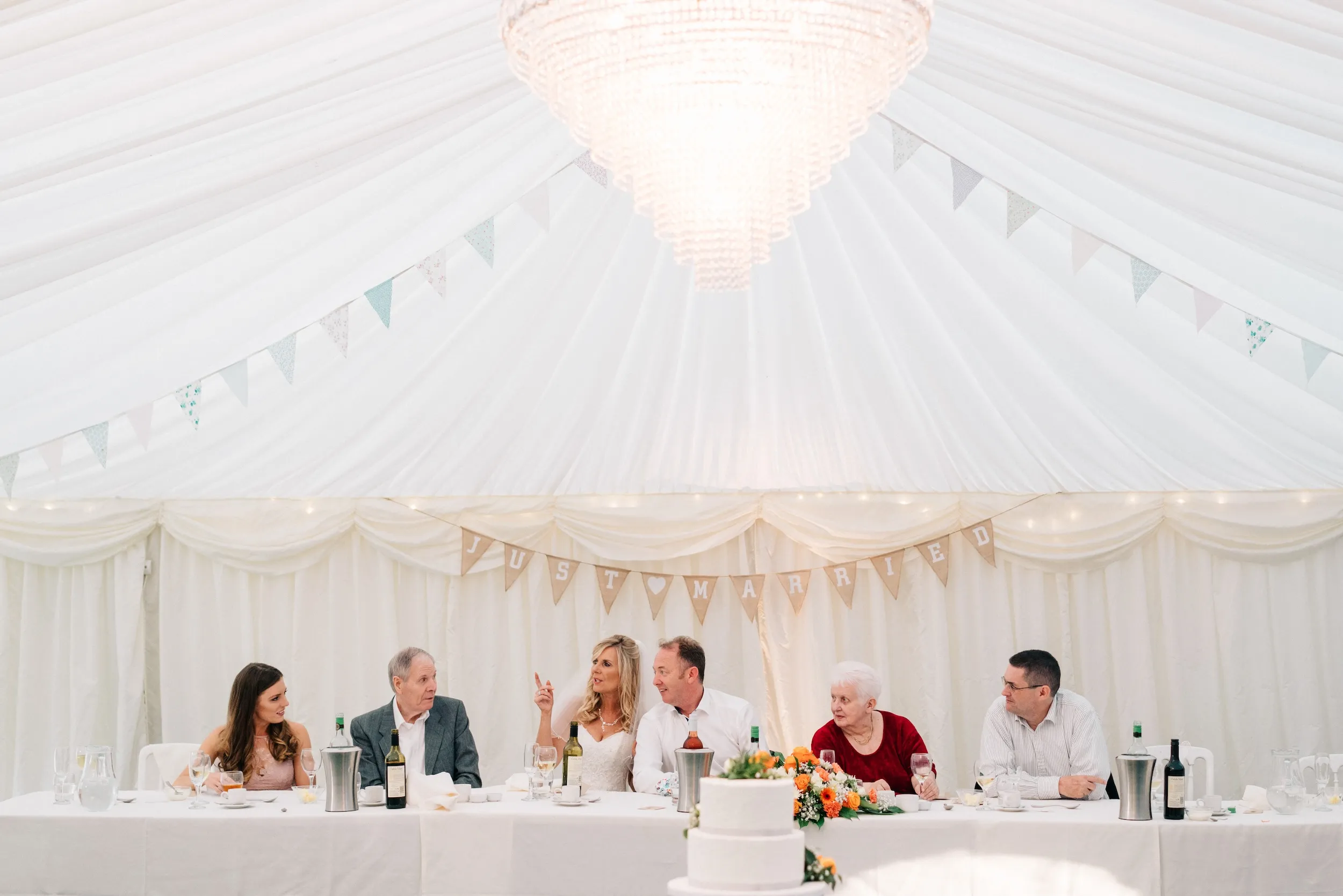 A wider view of the top table under the marquee chandelier and bunting