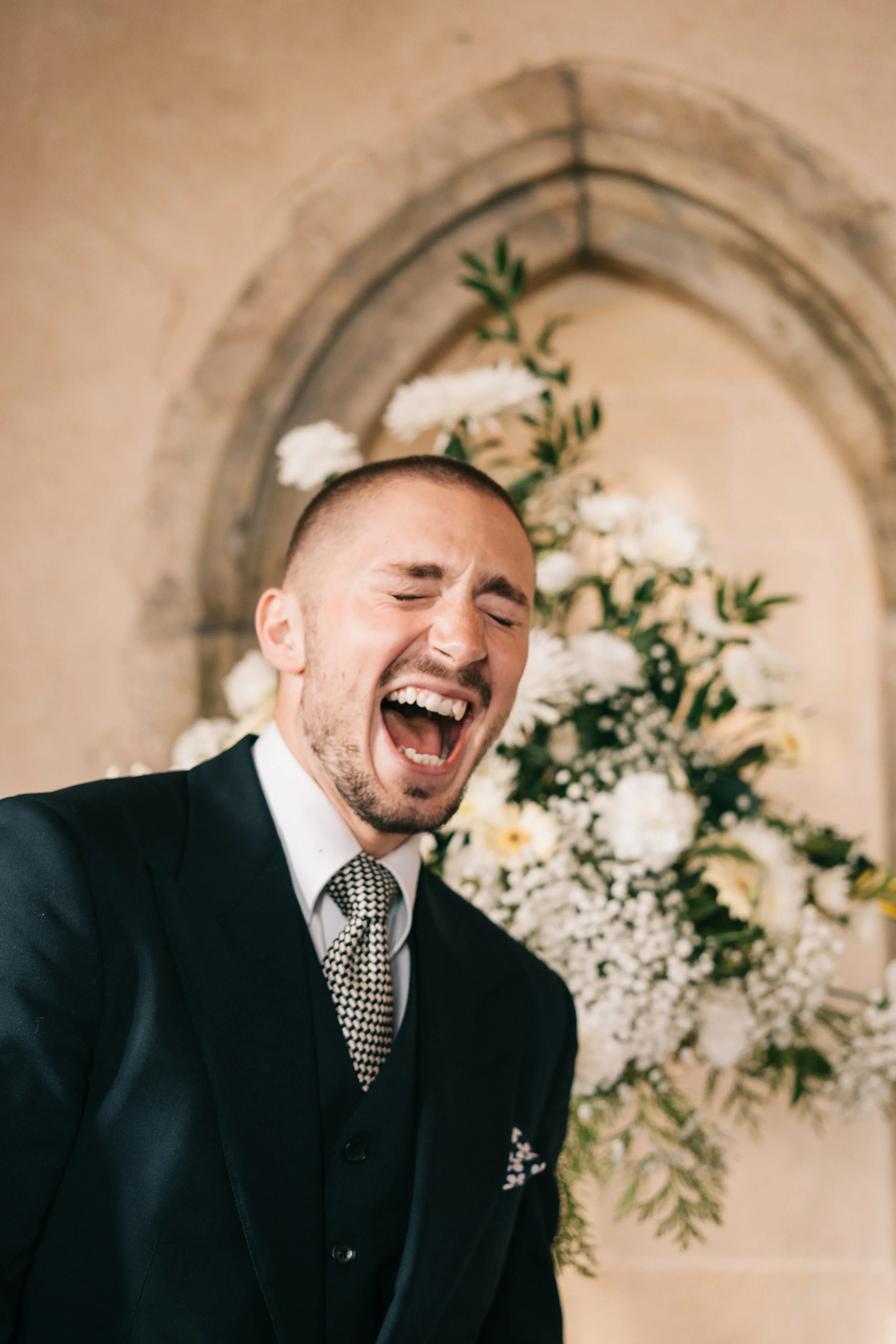 A guest in a three-piece suit laughs out loud beside the flowers in the Great Hall